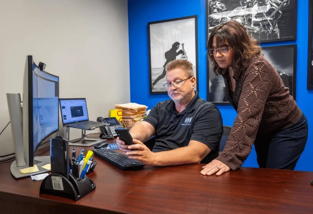 MIS Solutions IT support team collaboratively reviewing a mobile device, demonstrating proactive monitoring and cybersecurity